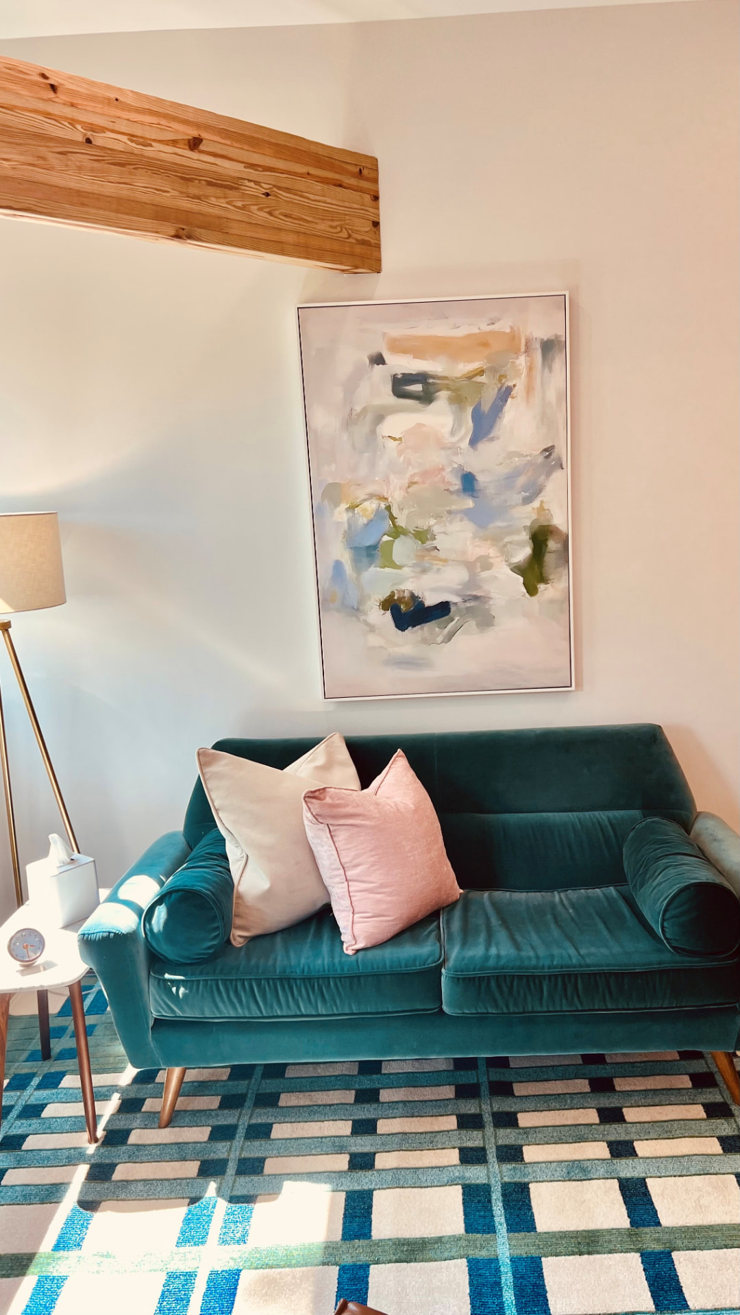 A green velvet sofa beneath abstract art and an exposed wood beam in a Dallas Therapy Associates office
