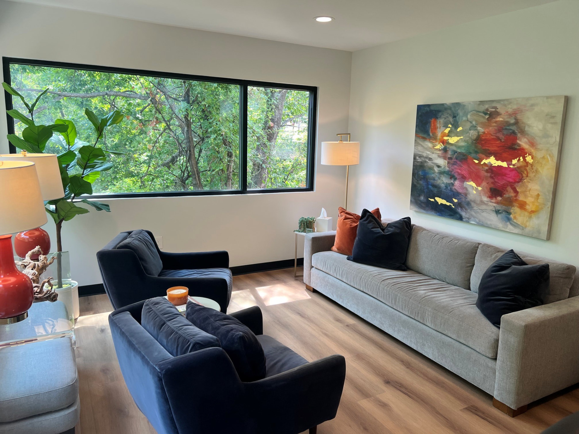 A Dallas Therapy Associates therapy room with a grey sofa, navy chairs, and a treetop window